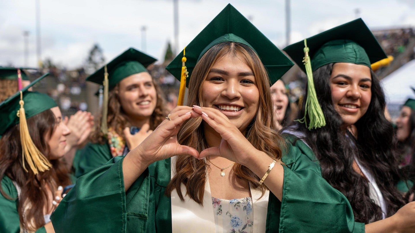 student success student in green graduation regalia using hands to form an O