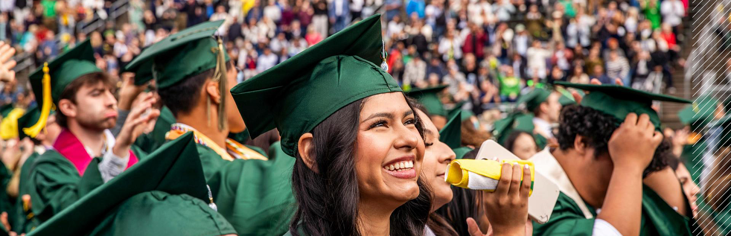 student smiling in crowd during commencement ceremony looking upwards