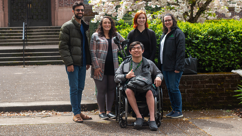 aec staff and student in wheelchair pose together outside in front of cherry blossom tree