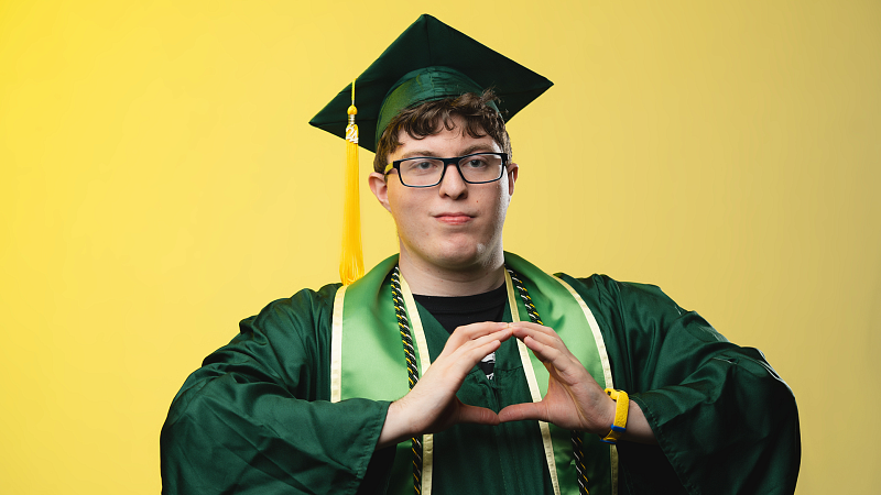 pathwayoregon student carter posing in his graduation regalia and displaying hand symbol 'o'