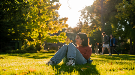 student sitting in grass during sunset with headphones in